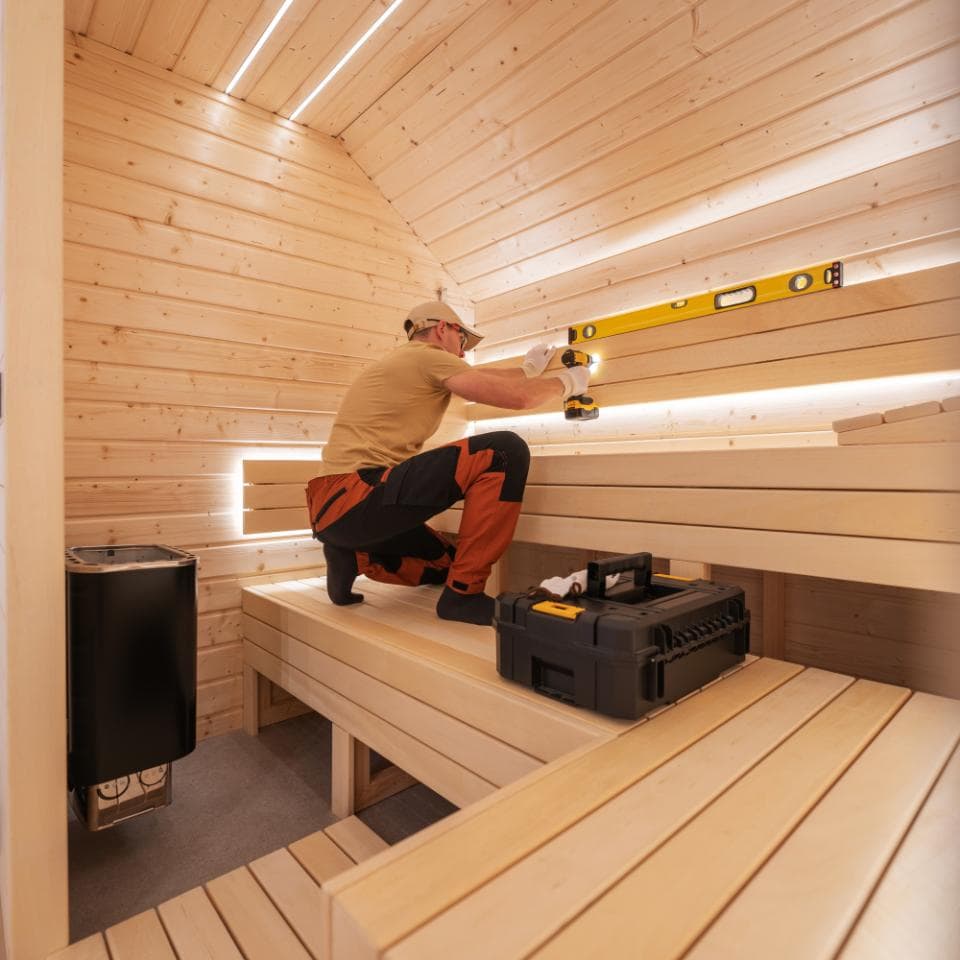 Handyman installing LED lighting in a modern cedar sauna, working with power tools for home wellness setup, promoting relaxation and health benefits of sauna therapy.